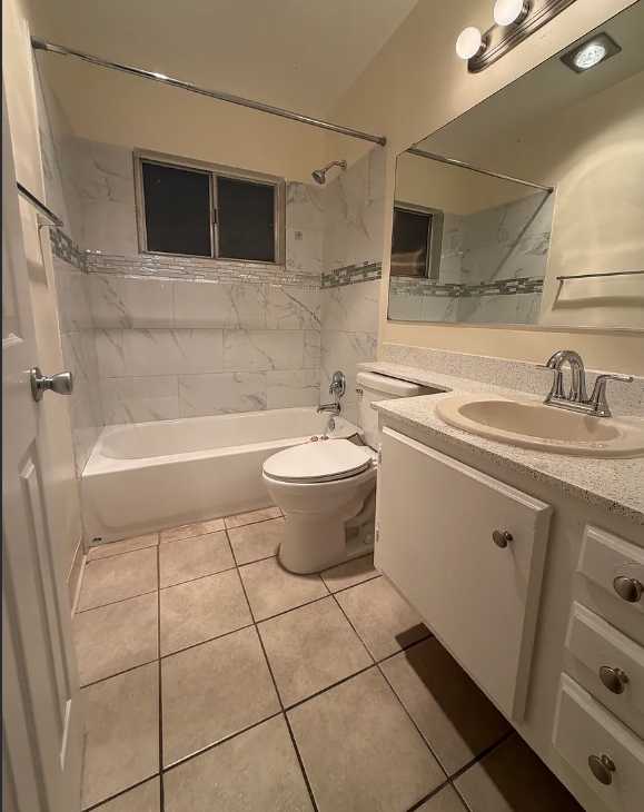 A white toilet sits in a bathroom next to a sink and a bathtub.